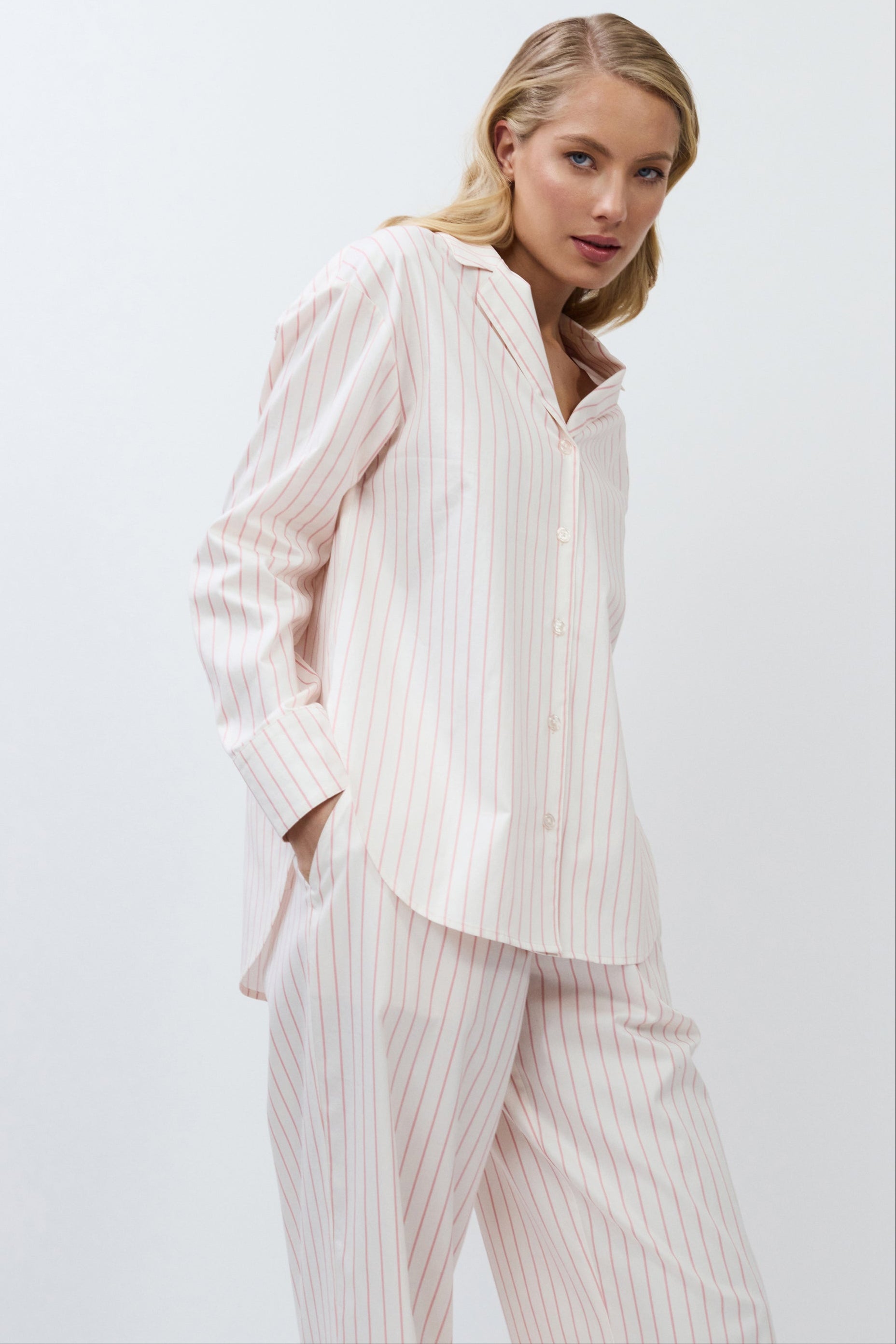 Woman wearing a light pink striped pajama set against a white background
