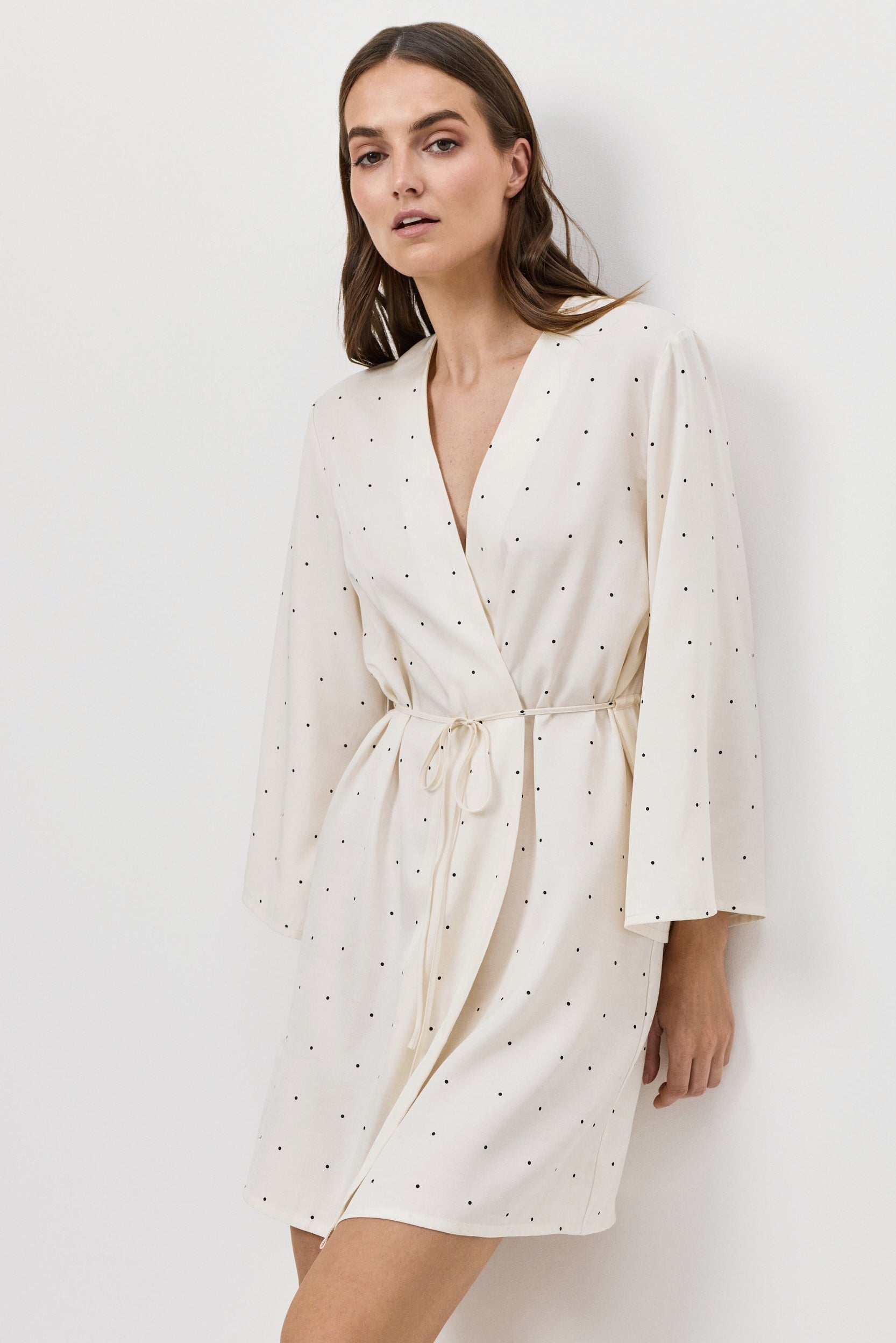 Woman wearing a white polka dot gown against a plain background