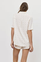 Woman wearing a white polka dot pajama set with shorts on a plain background