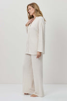 Woman wearing a white outfit with wide-leg pants against a plain background