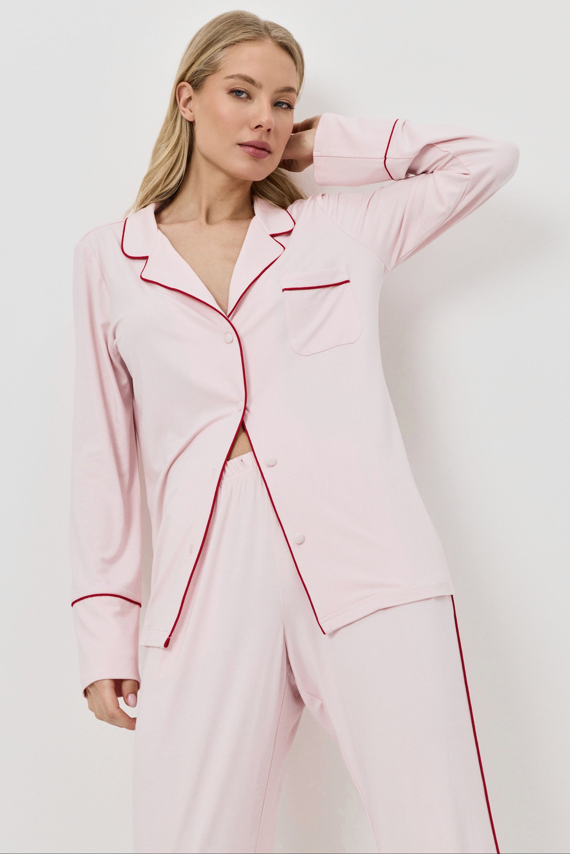 Woman wearing a pink pajama set with red piping on a white background