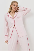 Woman wearing a pink pajama set with red piping on a white background