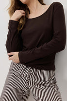 Woman wearing a dark brown top and black and white striped pants against a light background