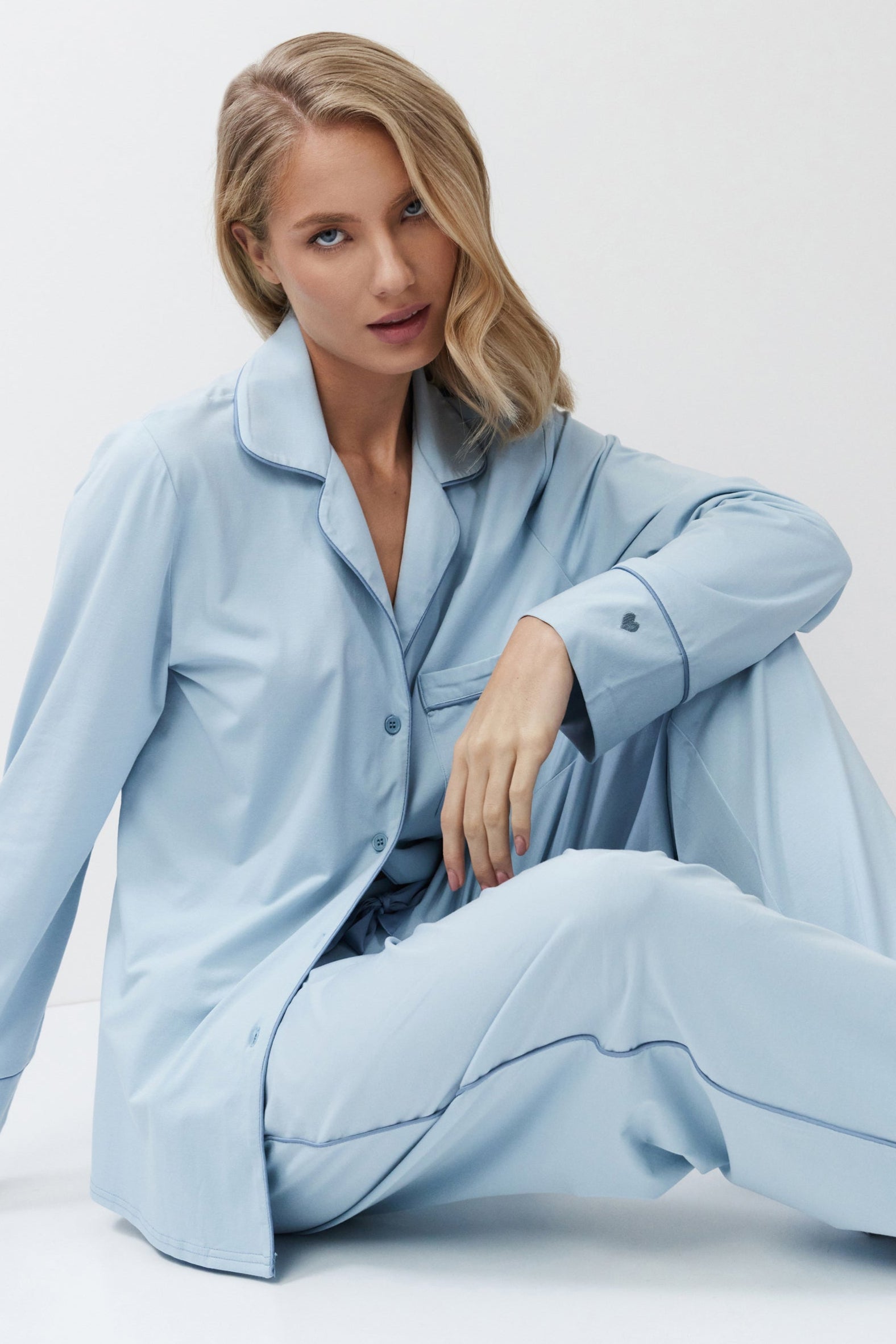 Woman wearing a light blue pajama set sitting on a white background