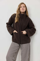 Woman wearing a brown jacket and striped pants against a white background