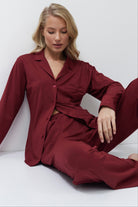 Woman wearing a burgundy pajama set sitting on a white floor.