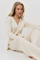 Woman wearing a white ribbed pajama set with pants sitting on a white background