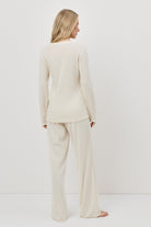 Woman wearing a white pajama set with pants standing against a white background