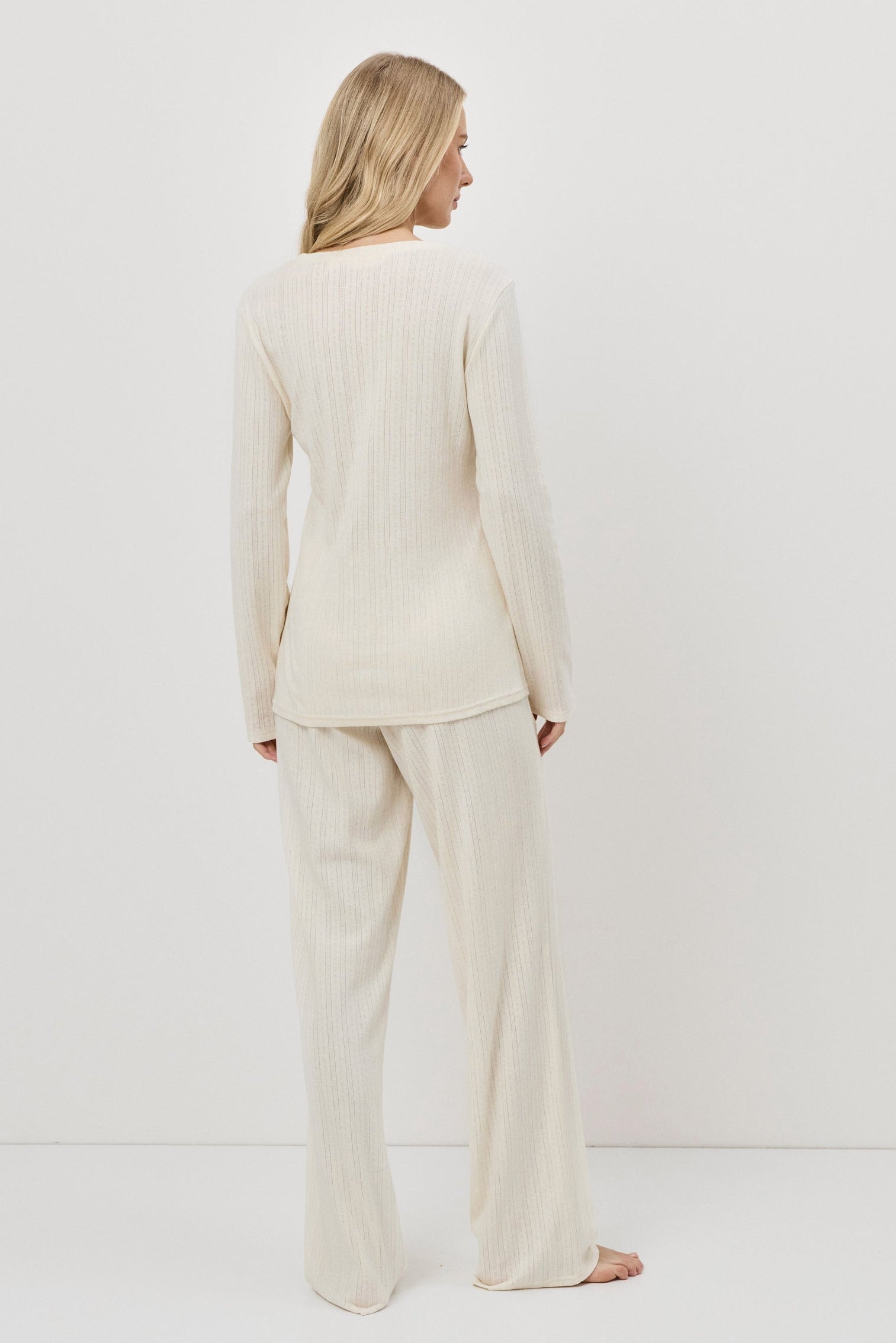 Woman wearing a white pajama set with pants standing against a white background