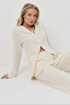 Woman wearing a white pajama set with pants sitting on a white background