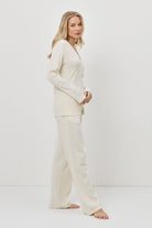 Woman wearing a cream-colored pajam set with pants against a white background