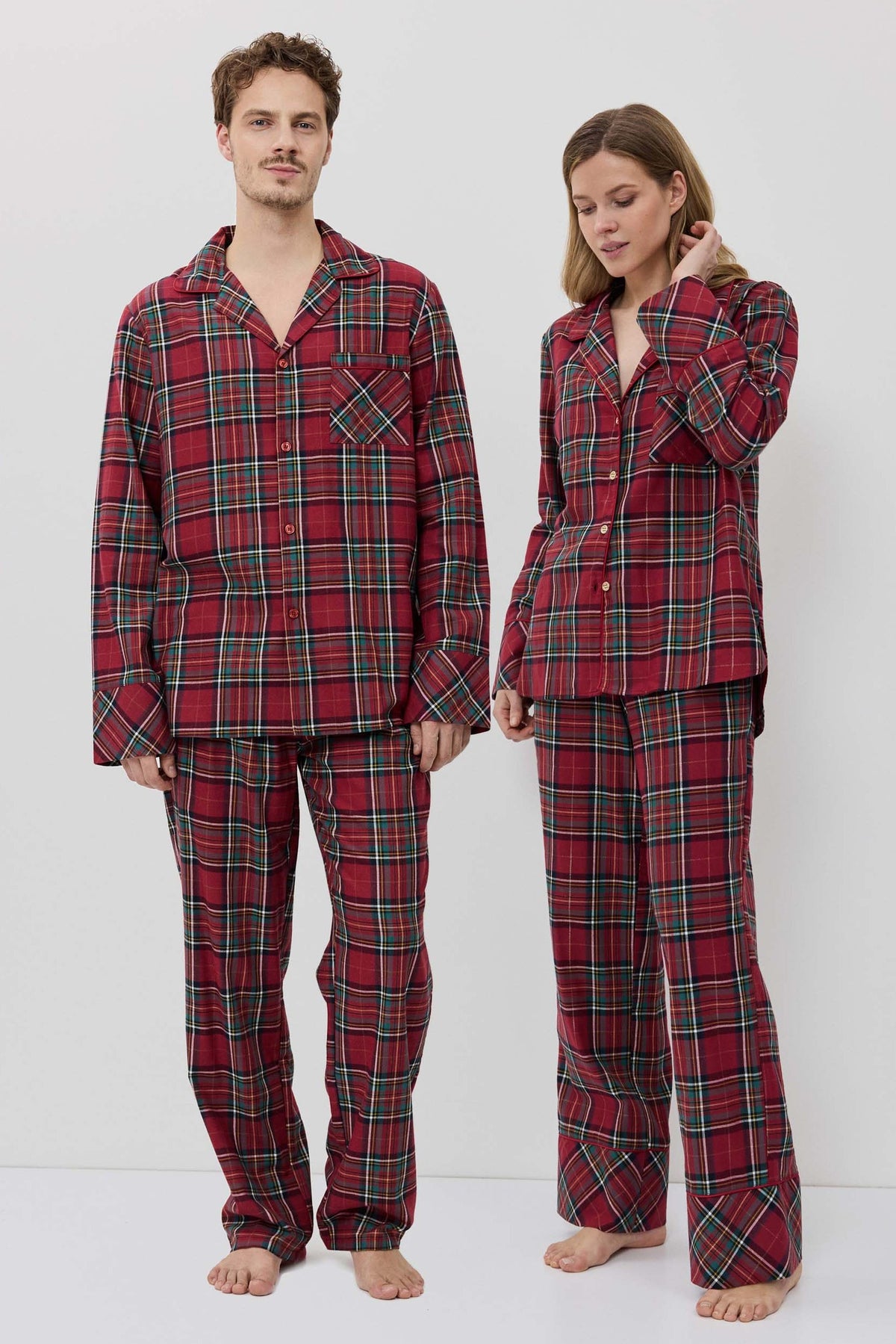 Two people wearing red plaid pajamas standing against a white background