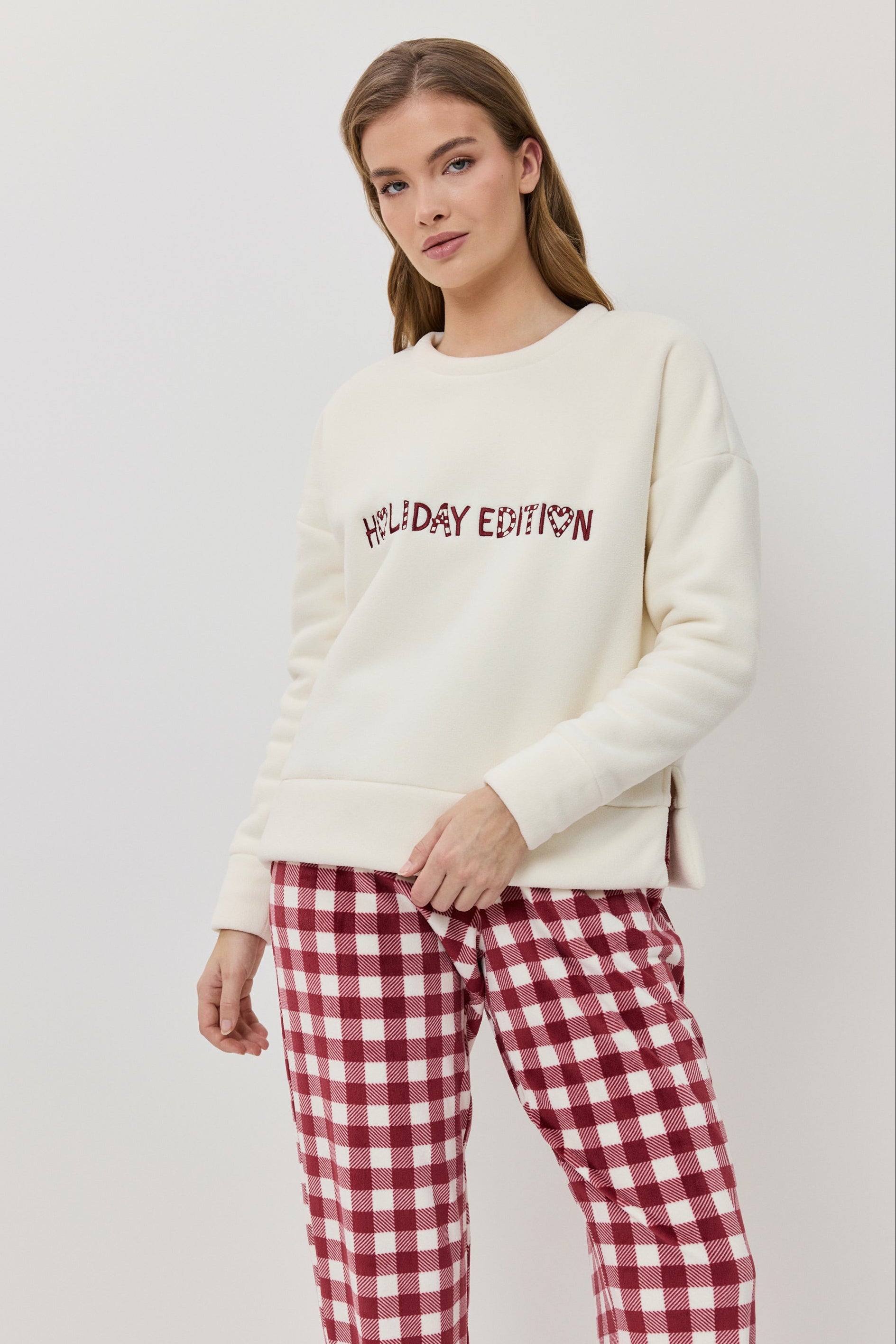Woman wearing a cream sweater with 'Holiday Edition' text and red plaid pants on a white background