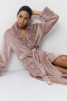 Woman wearing a plush pink robe against a white background