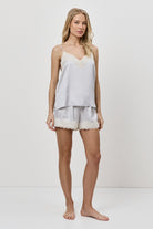 Woman wearing a light gray lace-trimmed pajama set on a white background