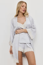 Woman wearing a light gray gown with lace trim over a matching pajama set on a white background