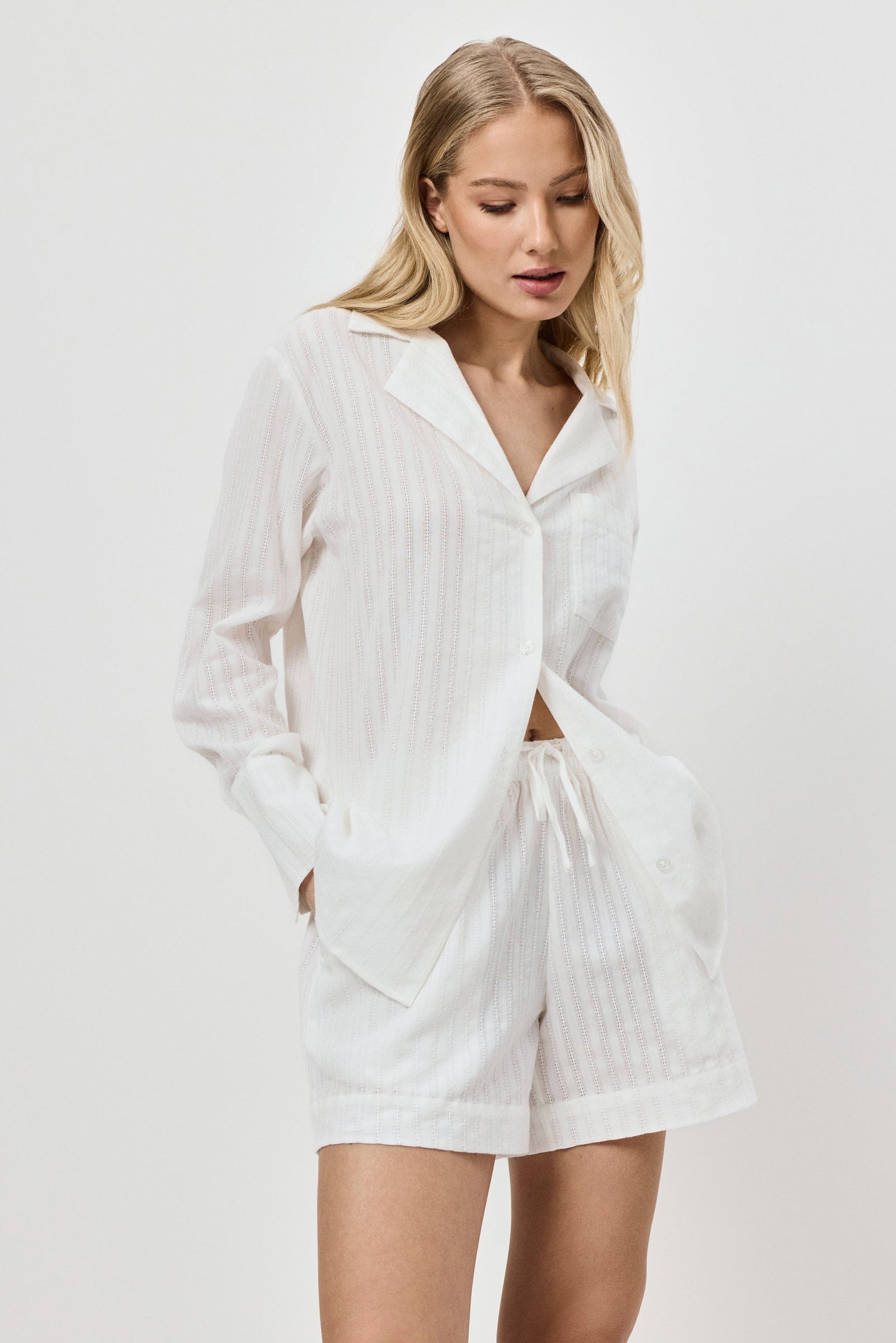 Woman wearing a white textured resort wear shirt and shorts set on a plain background