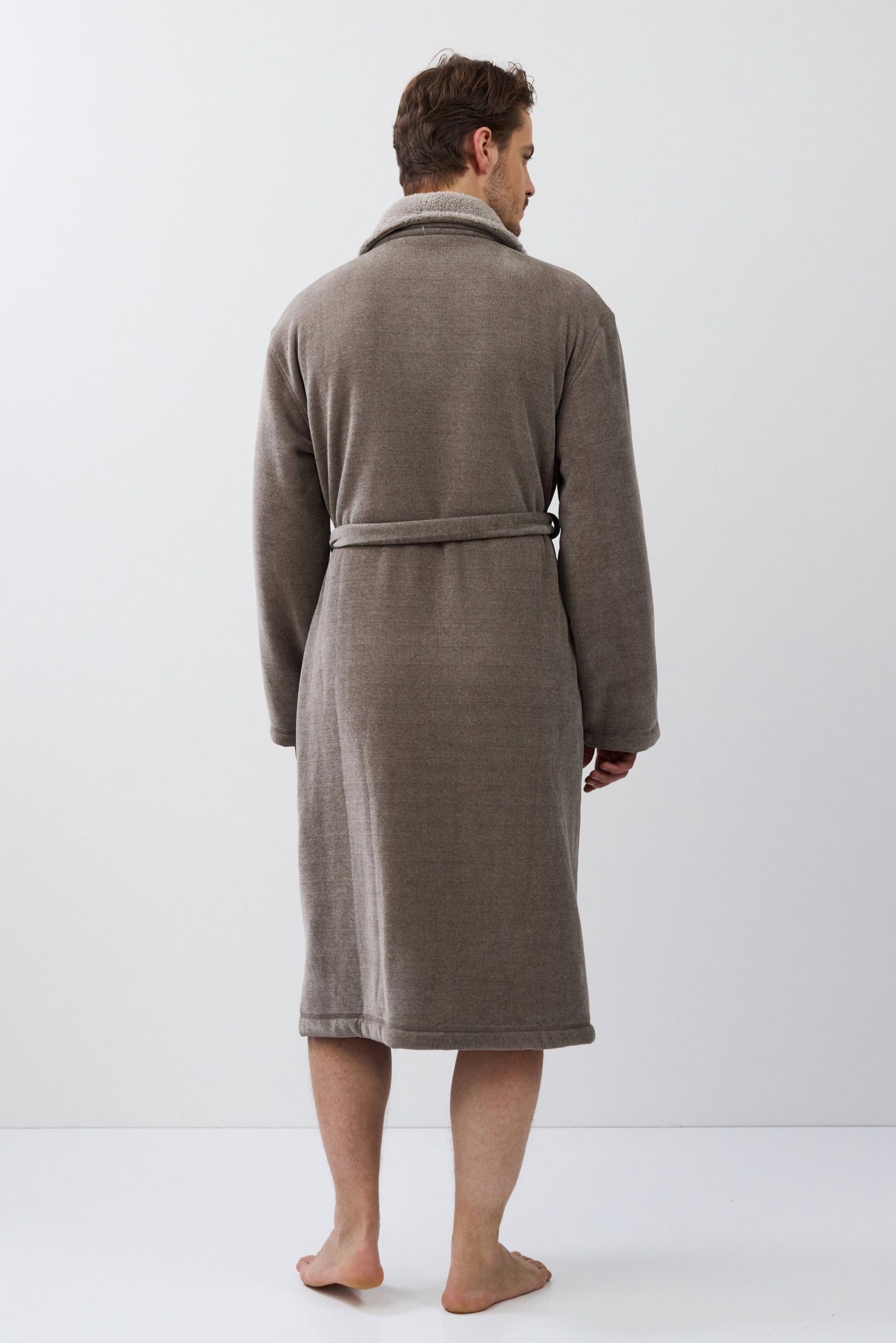 Man wearing a brown bathrobe standing against a white background