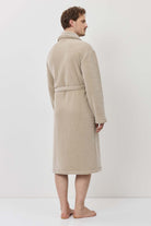 Person wearing a beige robe standing against a white background