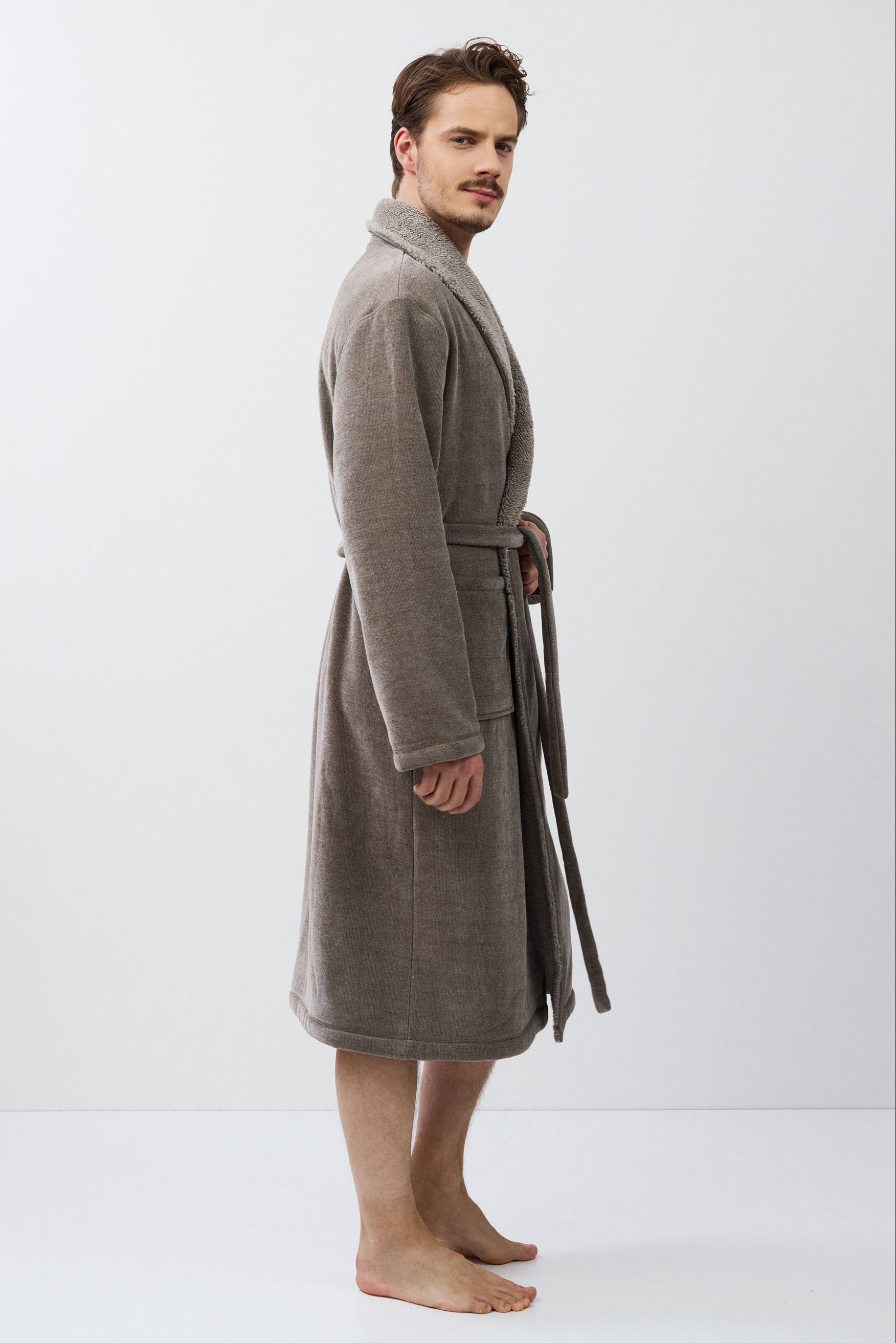 Man wearing a brown bathrobe standing against a white background
