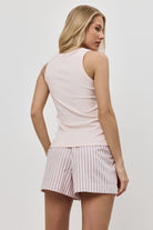 Woman wearing a light pink sleeveless top and striped pajama shorts on a plain background
