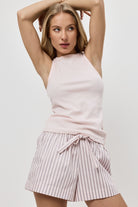 Woman wearing a pink sleeveless top and striped pajama shorts on a plain background