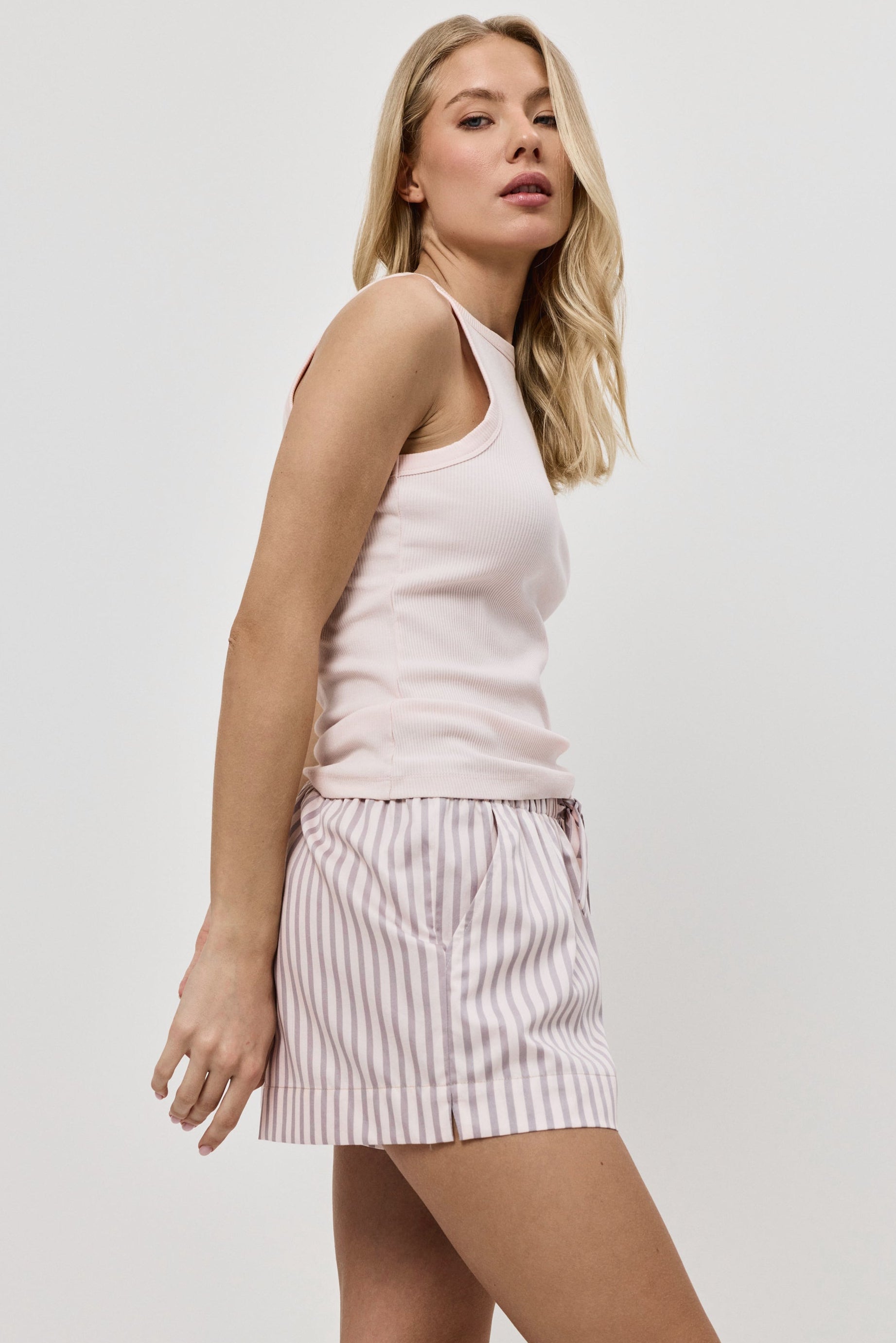 Woman wearing a light pink sleeveless top and striped pajama shorts on a white background