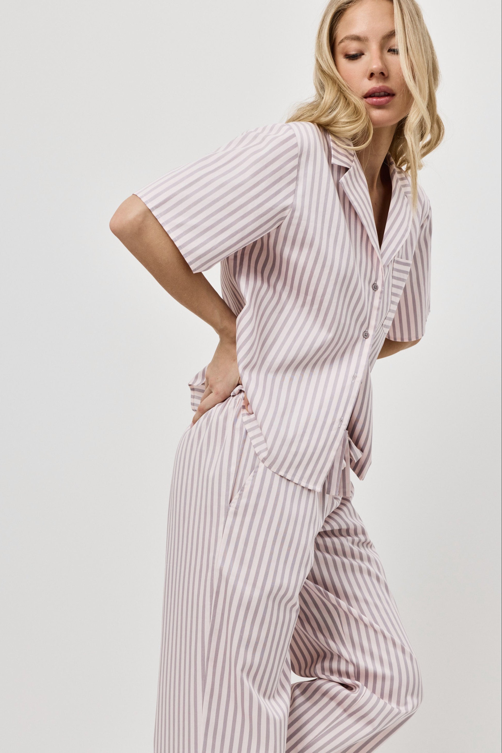 Woman wearing a pink striped pajama set on a plain background