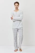 Man wearing a light gray long-sleeve shirt and plaid pajama pants on a white background