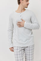 Man wearing a light gray long-sleeve shirt and plaid pajama pants on a plain background