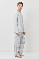 Man wearing a light gray long-sleeve shirt and checkered pants on a white background