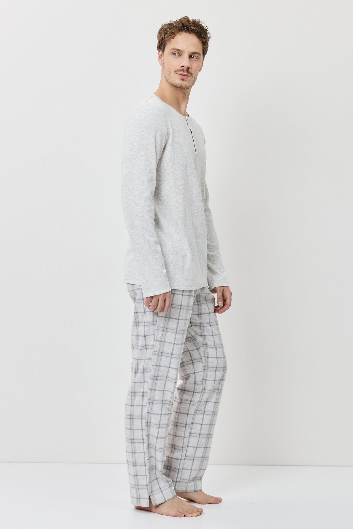 Man wearing a light gray long-sleeve shirt and checkered pants on a white background