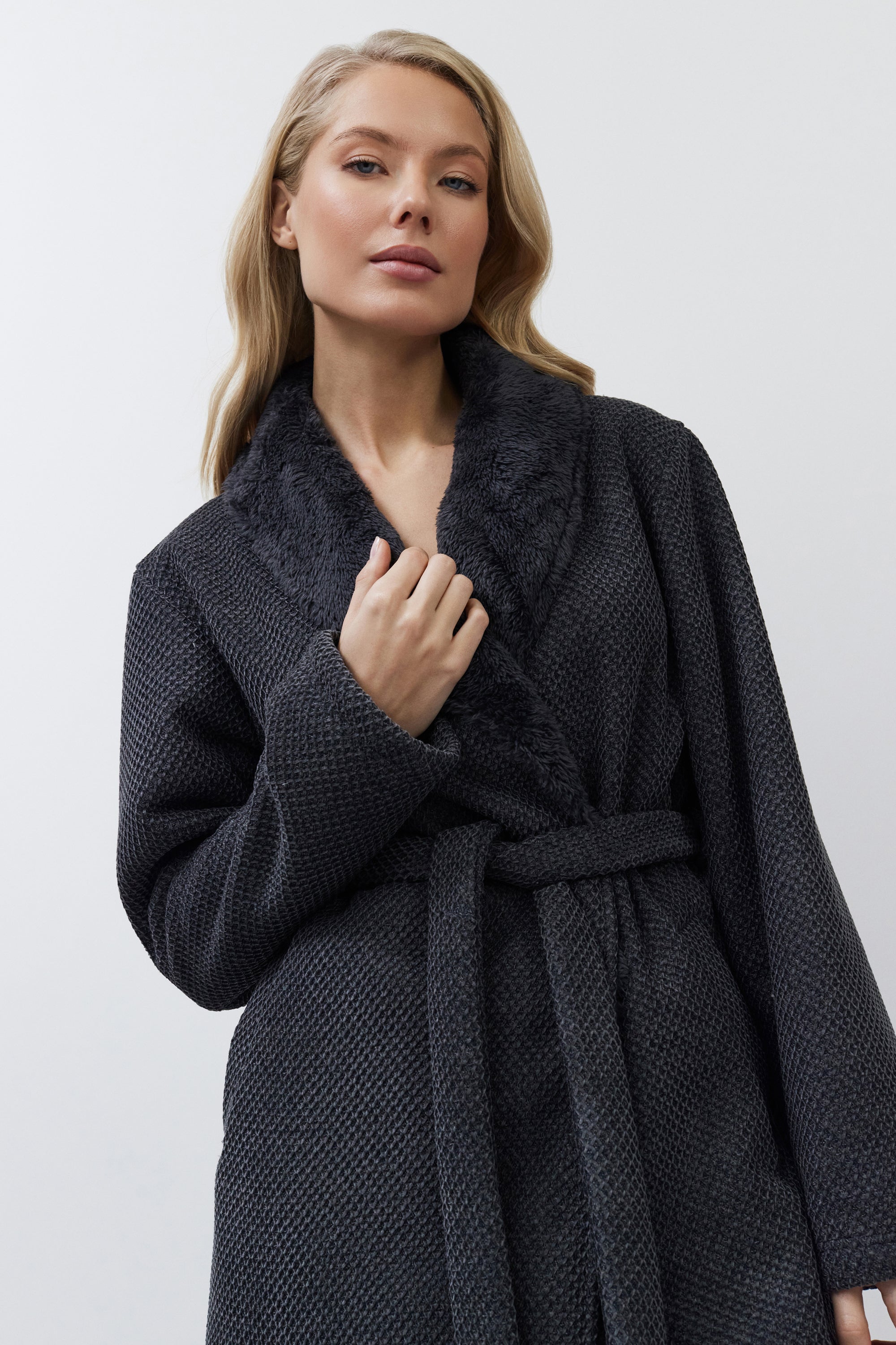 Woman wearing a dark gray textured bathrobe against a white background