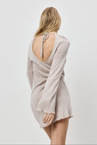 Woman wearing a beige dress with long sleeves and open back on a white background