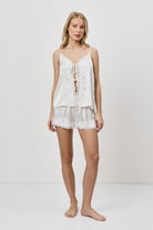 Woman wearing a white lace pajama top and shorts on a plain background