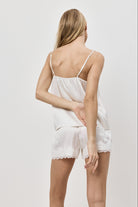 Woman wearing a white lace pajama set with shorts on a plain background