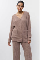 Woman wearing a brown knitted cardigan and pants on a white background