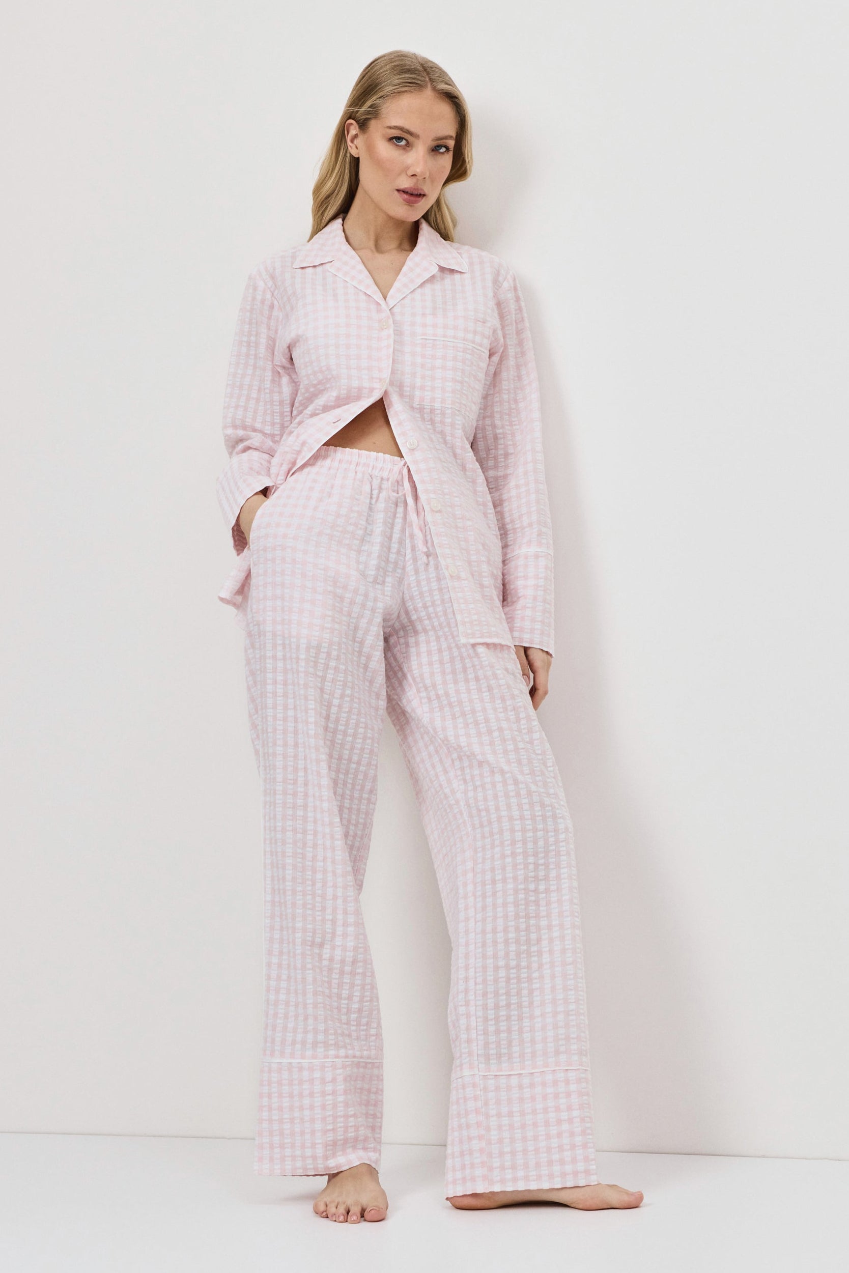 Woman wearing a pink checkered pajama set against a white background