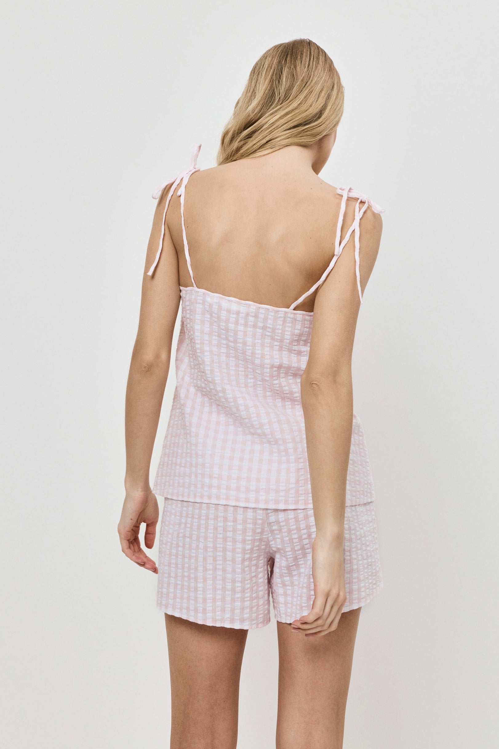 Woman wearing a pink checkered pajama set with thin straps on a white background