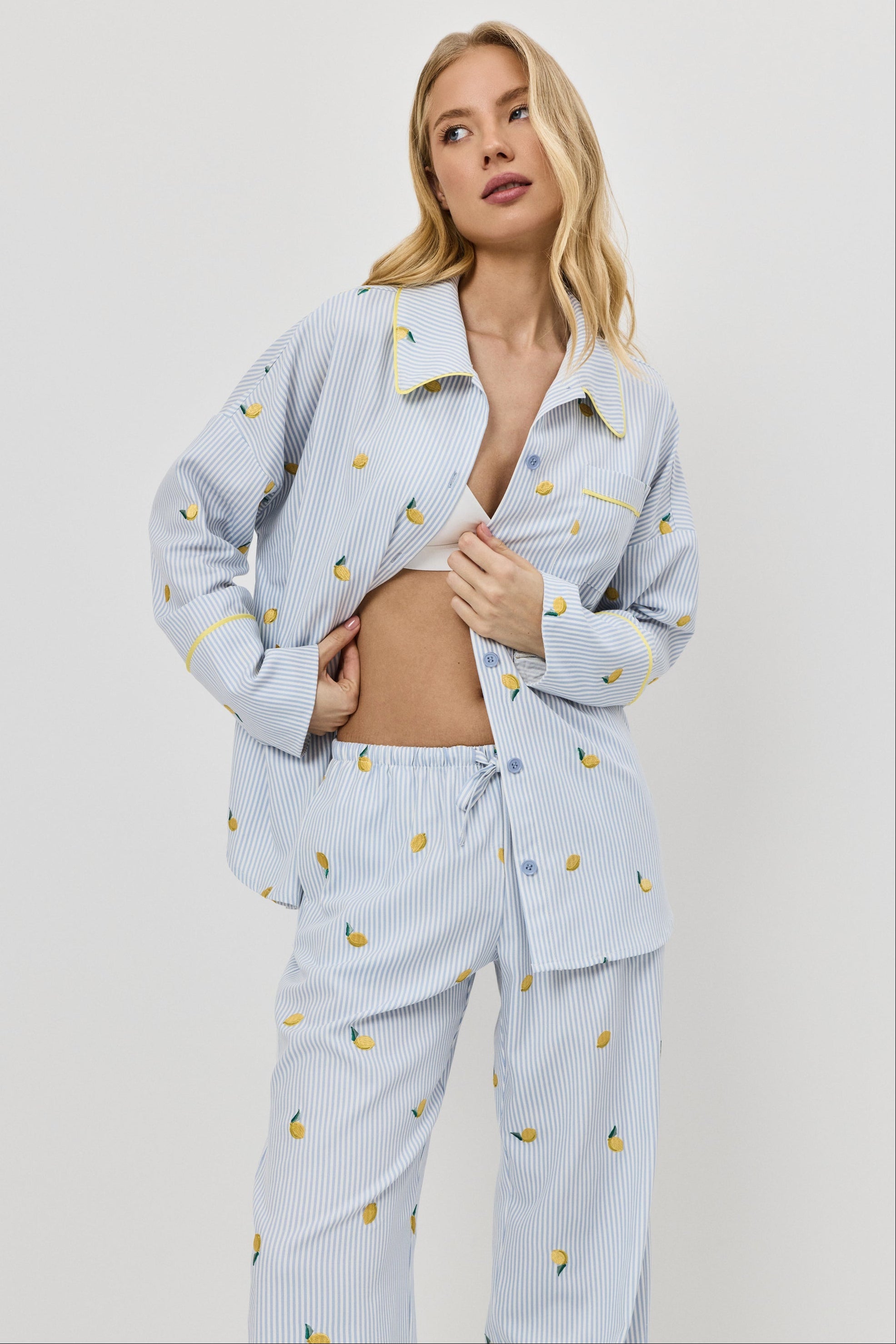 Woman wearing a light blue pajama set with lemon embroideries on a plain background