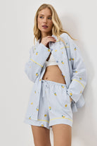 Woman wearing a light blue pajama set with lemon emroideries on a white background