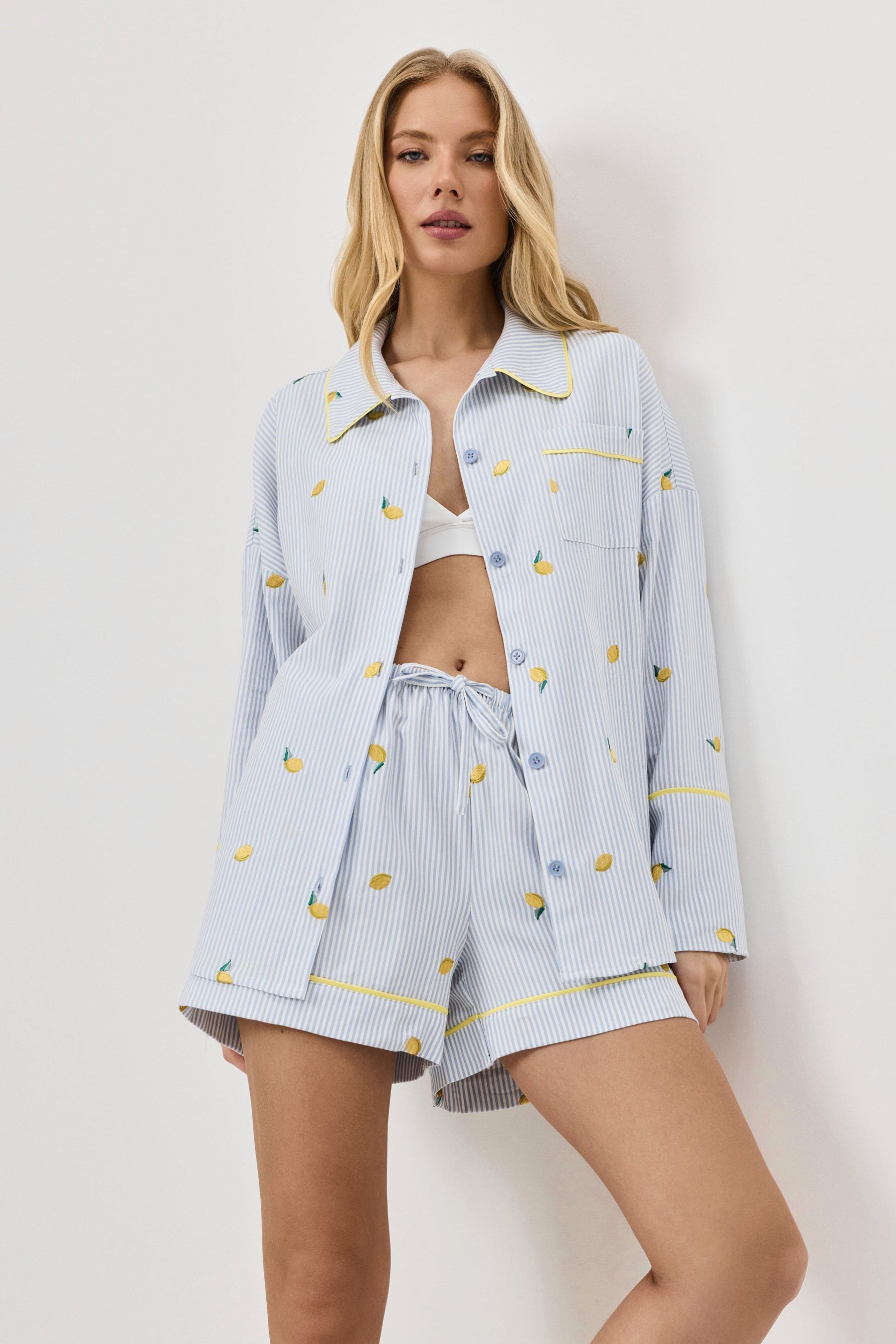 Woman wearing a light blue pajama set with lemon emroideries on a white background