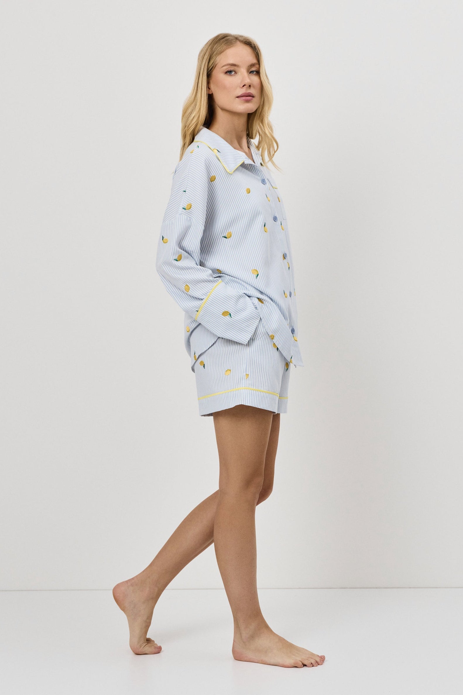 Woman wearing a light blue pajama set with lemon embroideeries on a white background