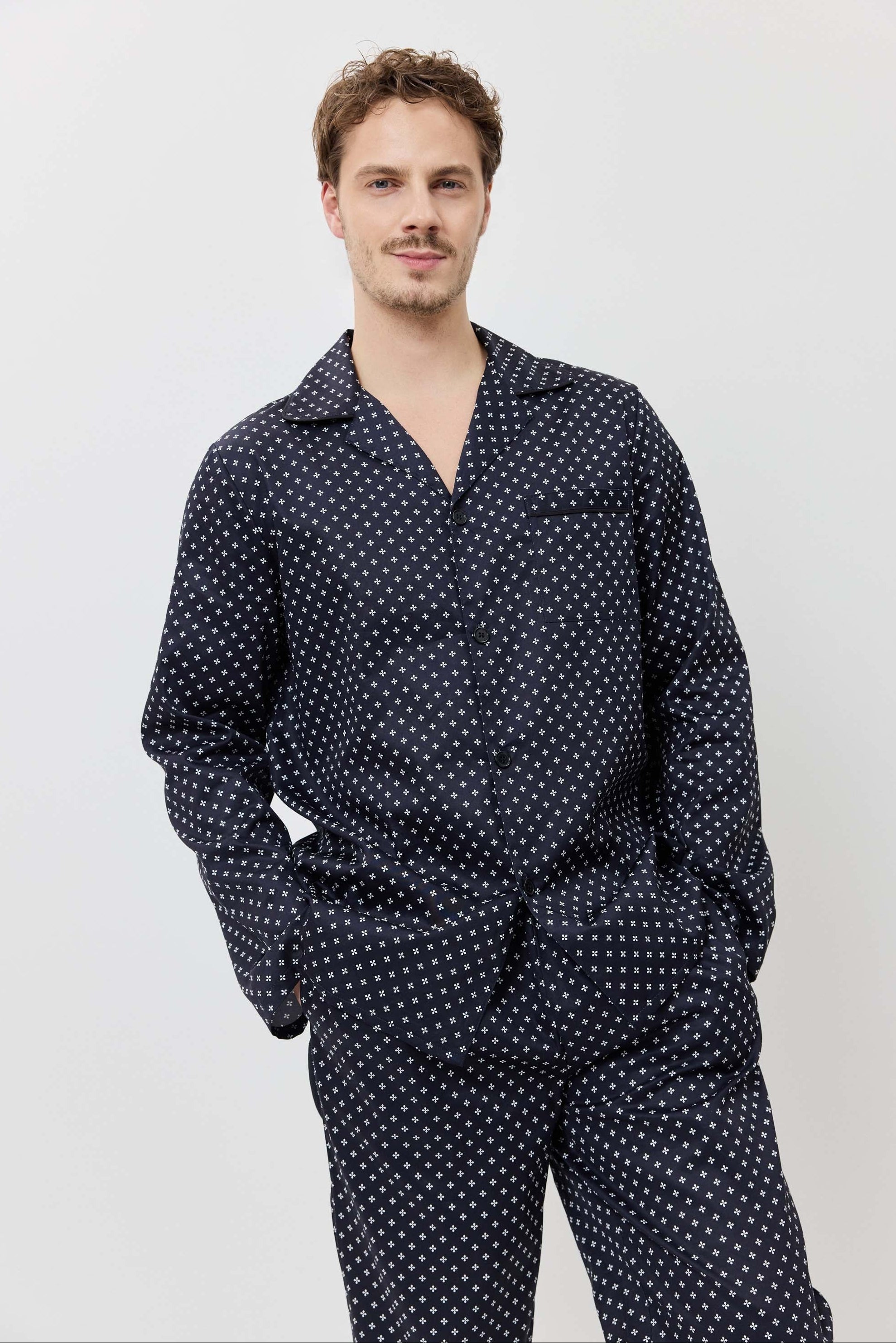 Man wearing a navy blue polka dot shirt and pants on a light gray background