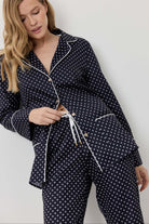 Woman wearing a navy blue polka dot pajama set against a white background