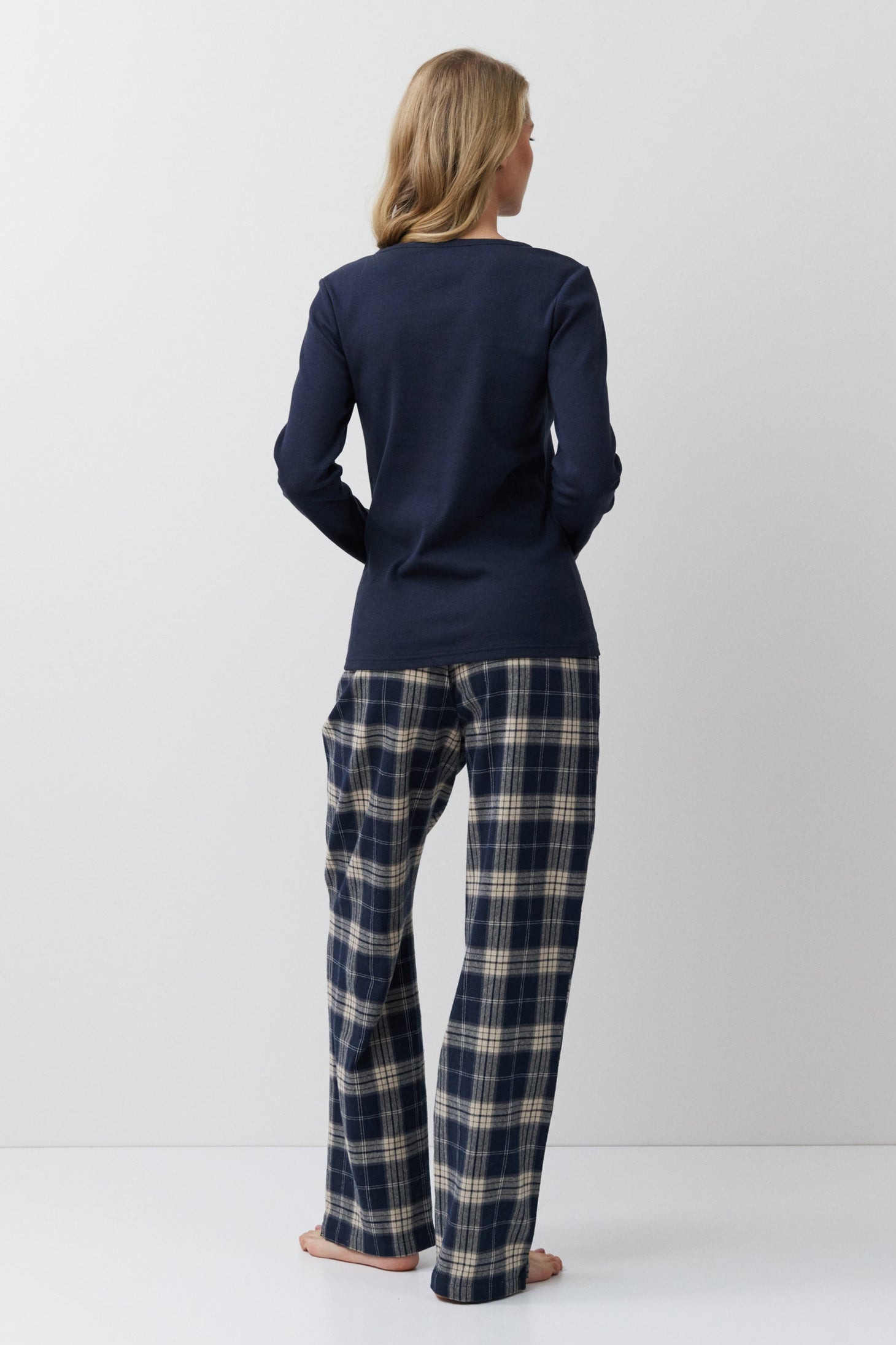 Person wearing a navy long-sleeve top and plaid pants on a white background