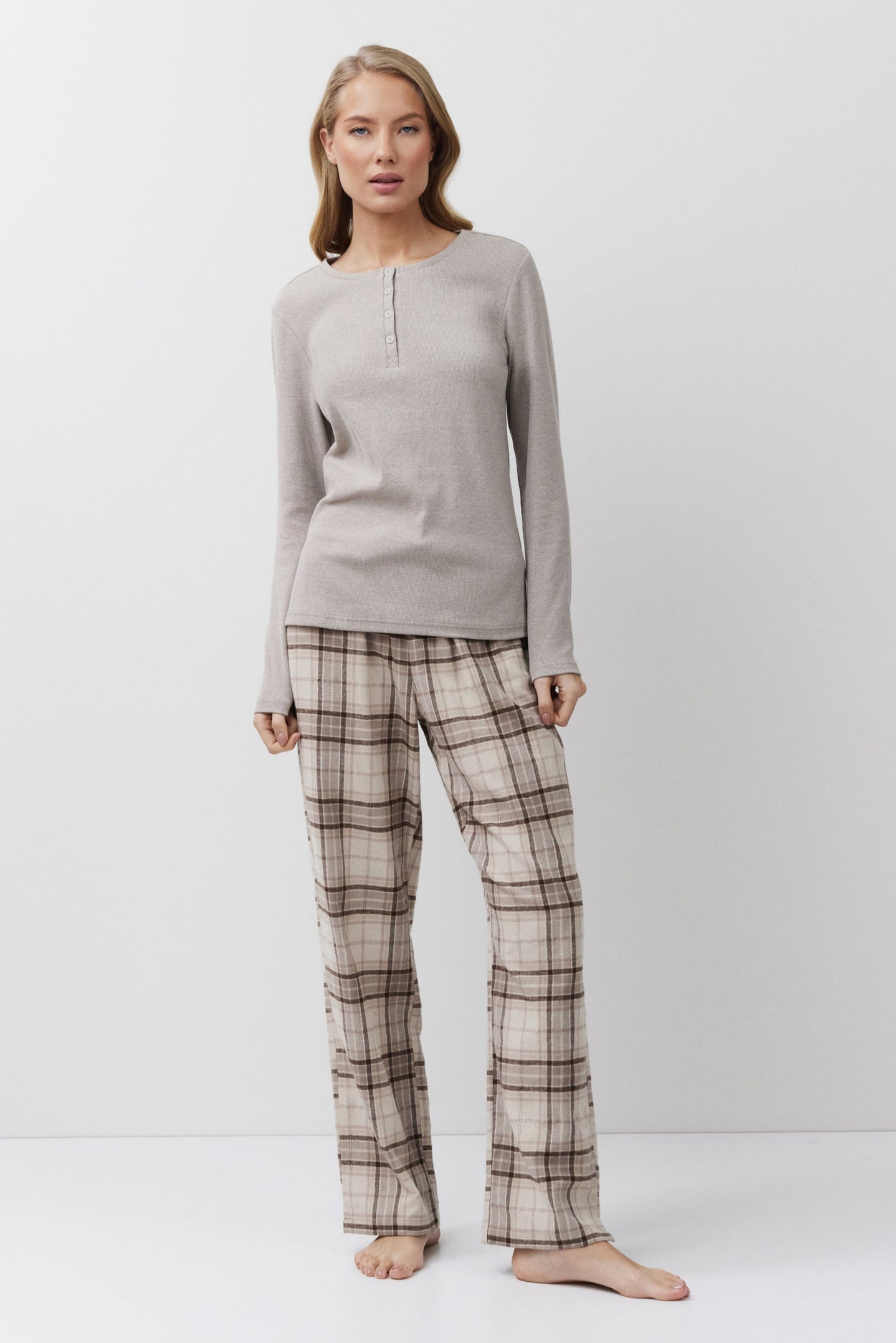 Woman wearing a beige long-sleeve top and plaid pants on a white background