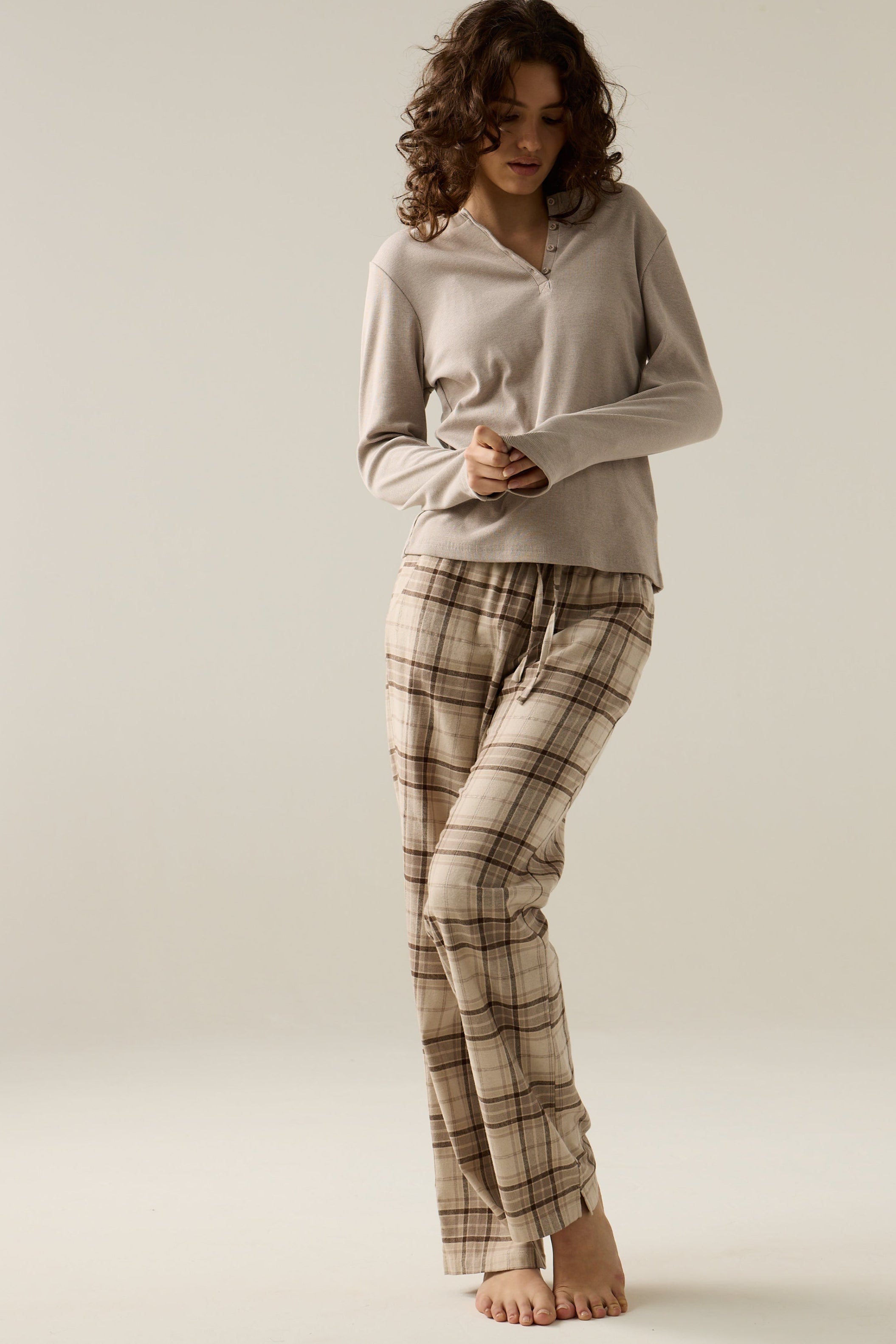Woman wearing a beige top and plaid pants on a plain background
