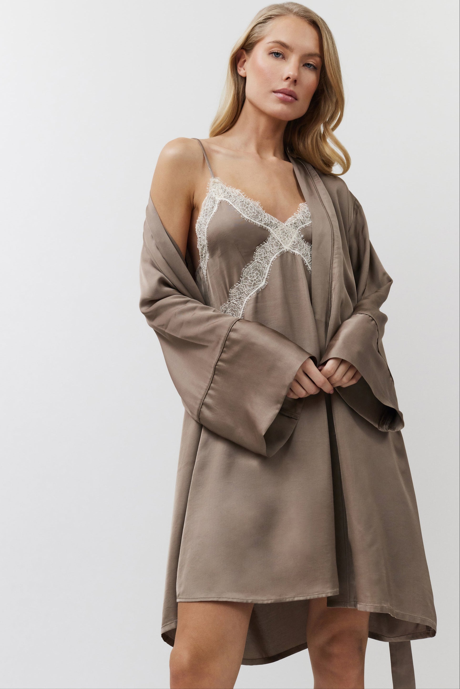 Woman wearing a brown gown over a matching nightdress with lace details on a white background