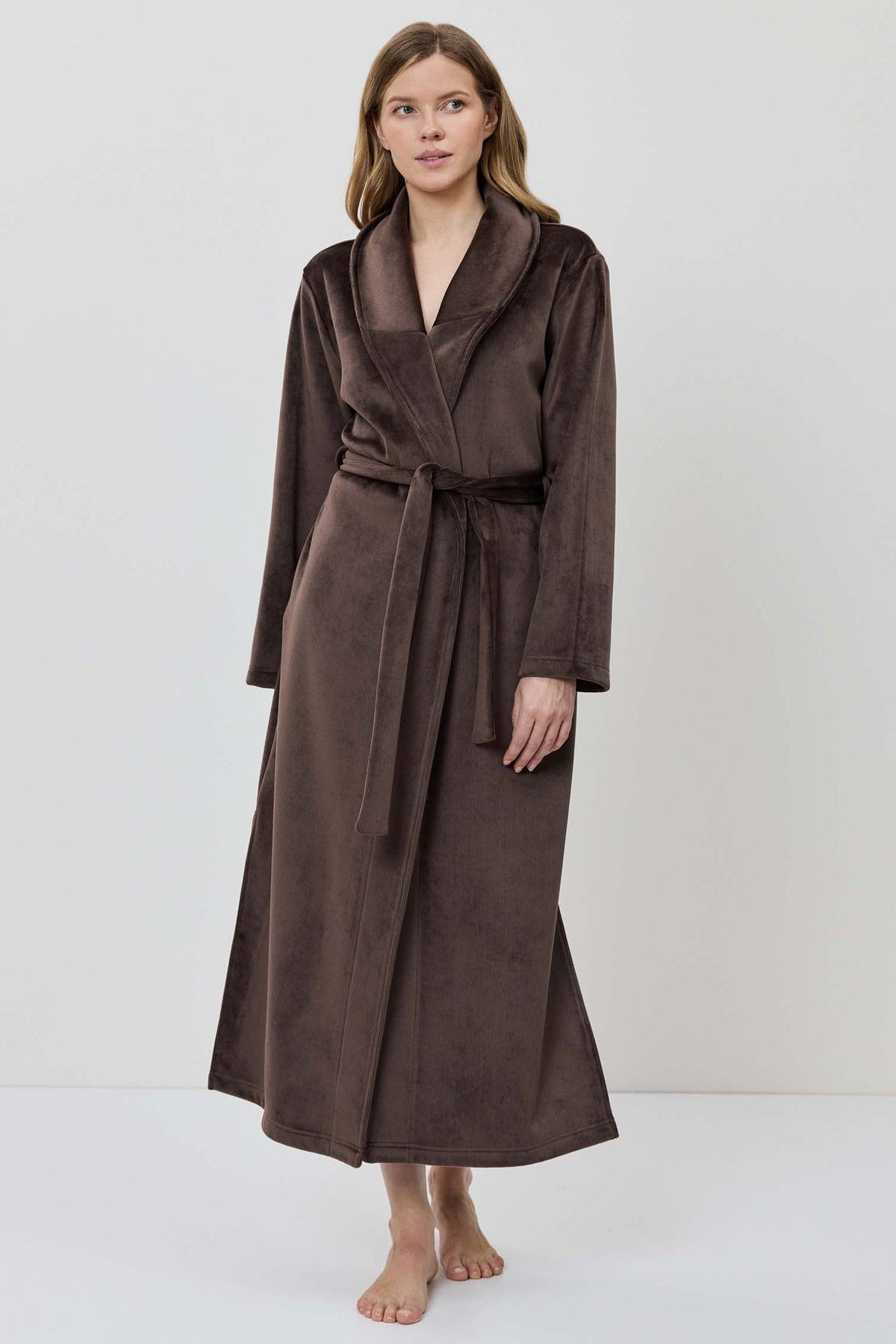 A woman wearing a long brown plush bathrobe with a tie belt.